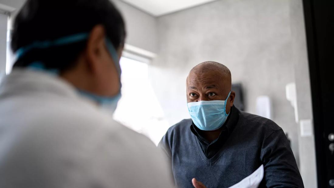 Doctor talking to a patient on medical appointment &#8211; using protective face mask