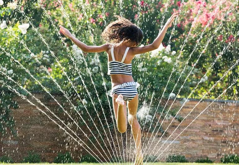 child runs through sprinkler during summer