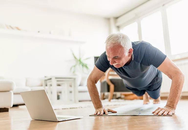 A person does pushups while watching their laptop screen.