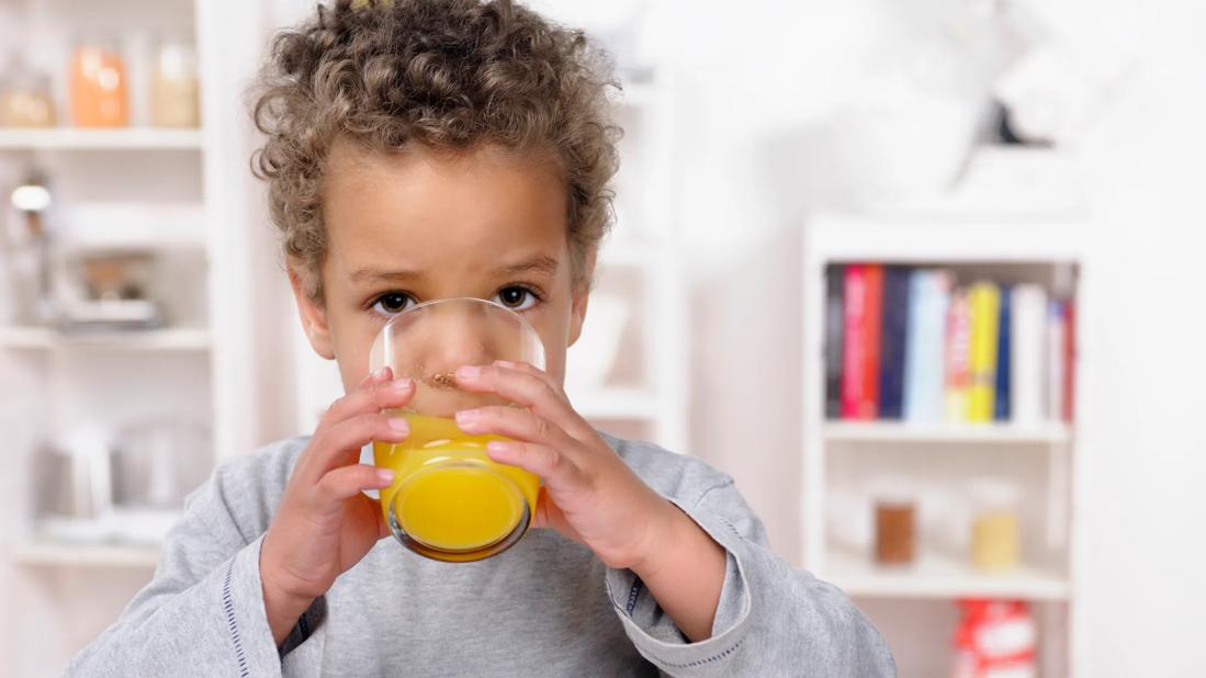 Toddler drinking orange juice from a glass