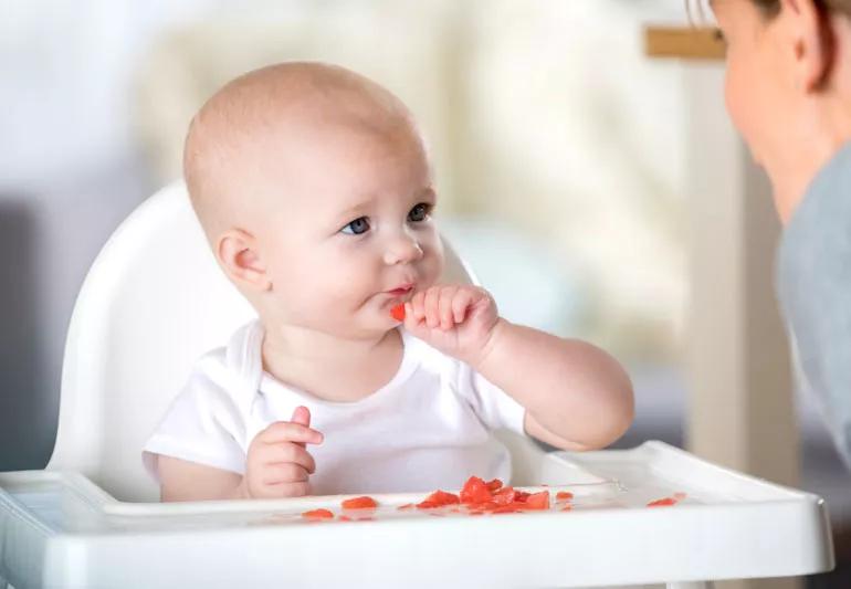 A baby eating fruit while sitting in a high chair