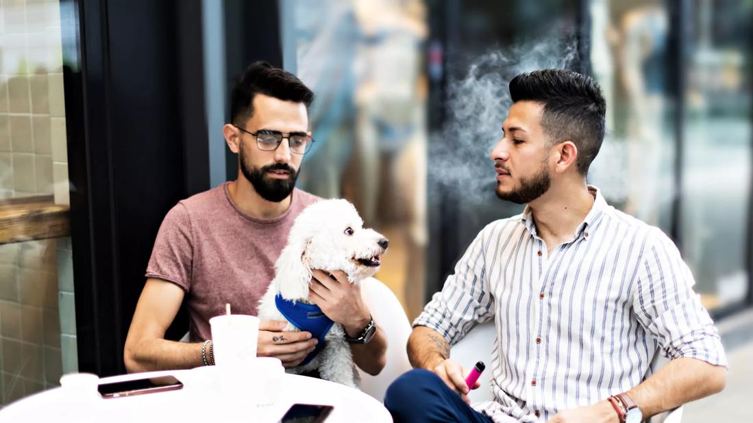 Young couple vaping at restaurant table outside.