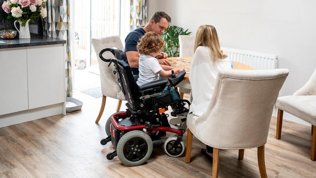 Family with young child in wheelchair putting together a puzzle at kitchen table