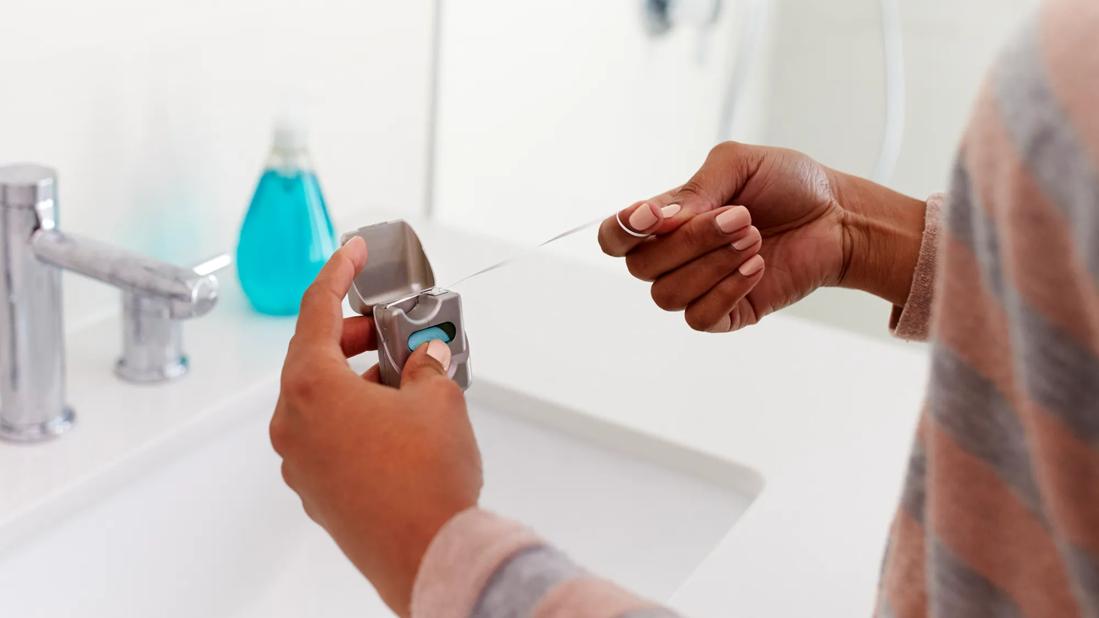 Person removing dental floss from container in bathroom