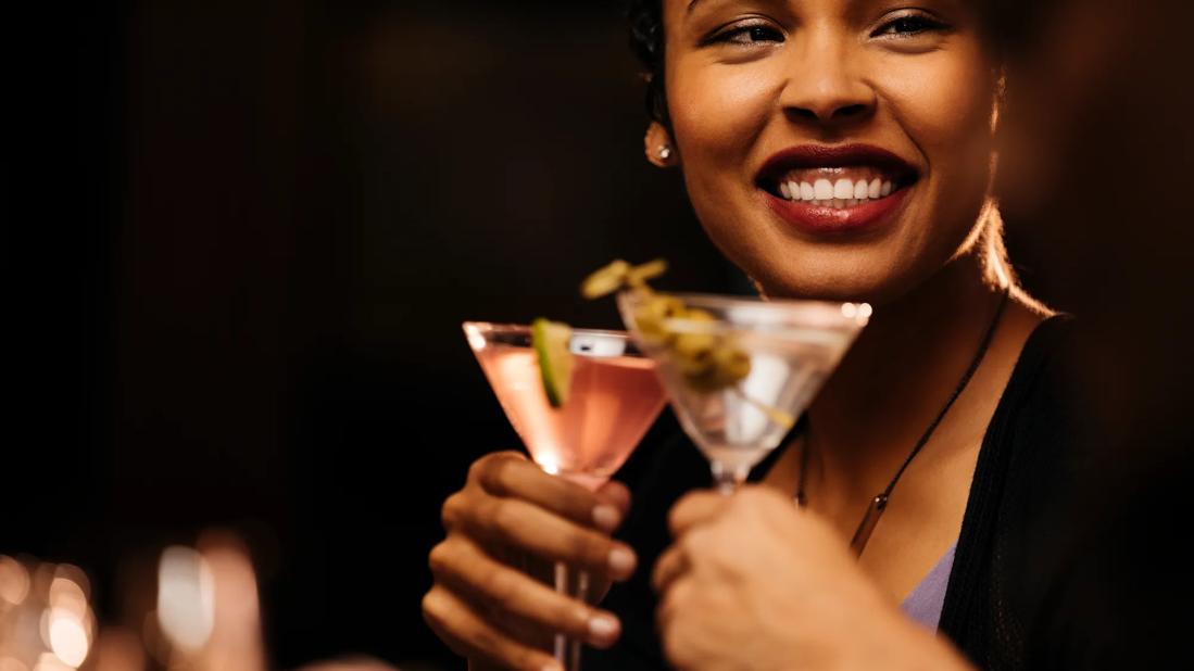 Smiling person holding martini glass, with another person's hand also holding maritini glass