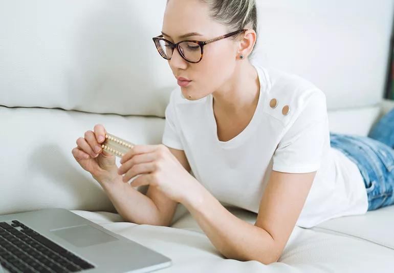 Woman looking at her birth control pills while on her laptop