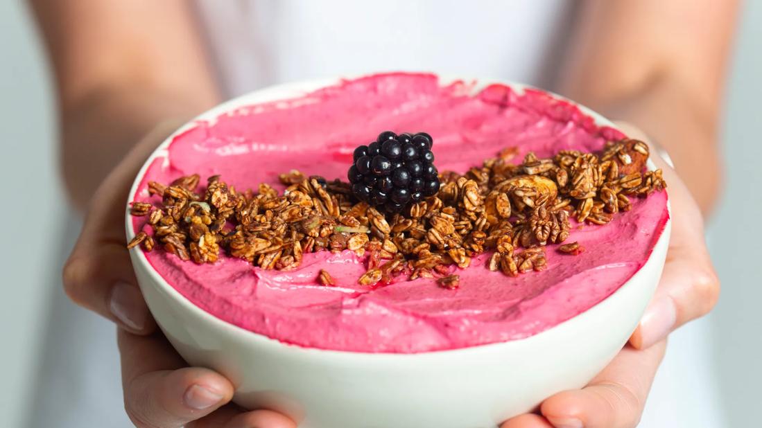 Hands holding a smoothie bowl with granola and a blackberry on top