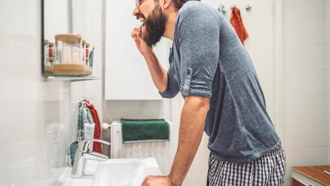 Bearded man brushing his teeth in home bathroom