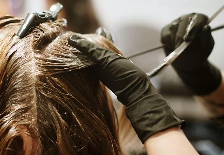 Stylist applying chemicals to head of hair.