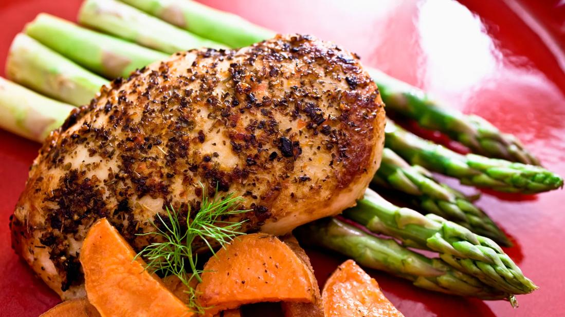 Grilled, seasoned chicken with asparagus and carrots on red plate