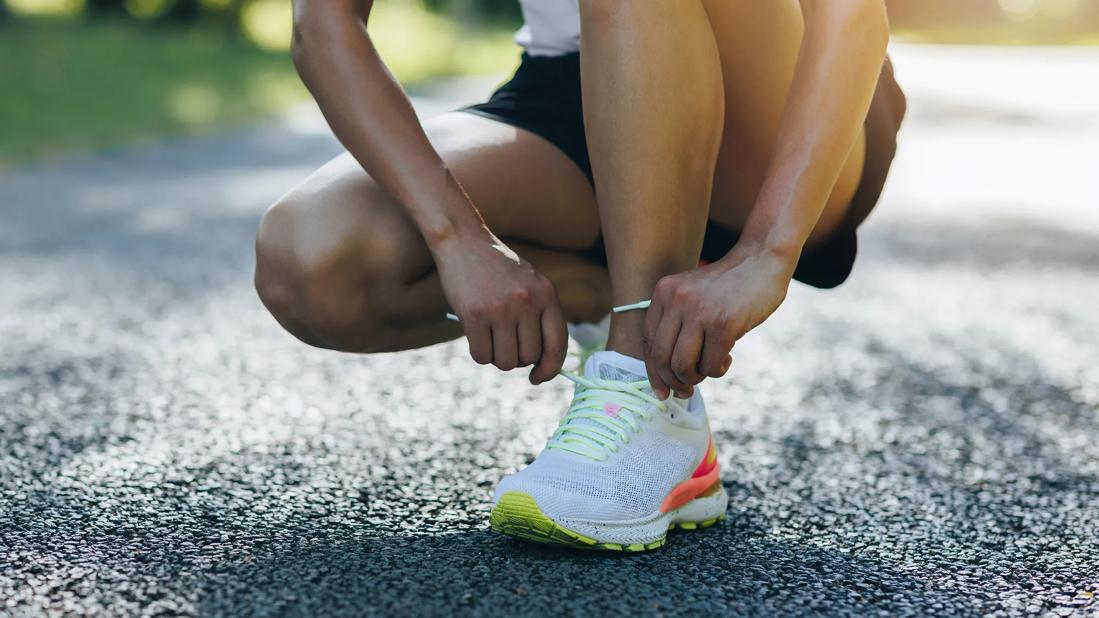 Person kneeled down tying running shoe on out door trail/track