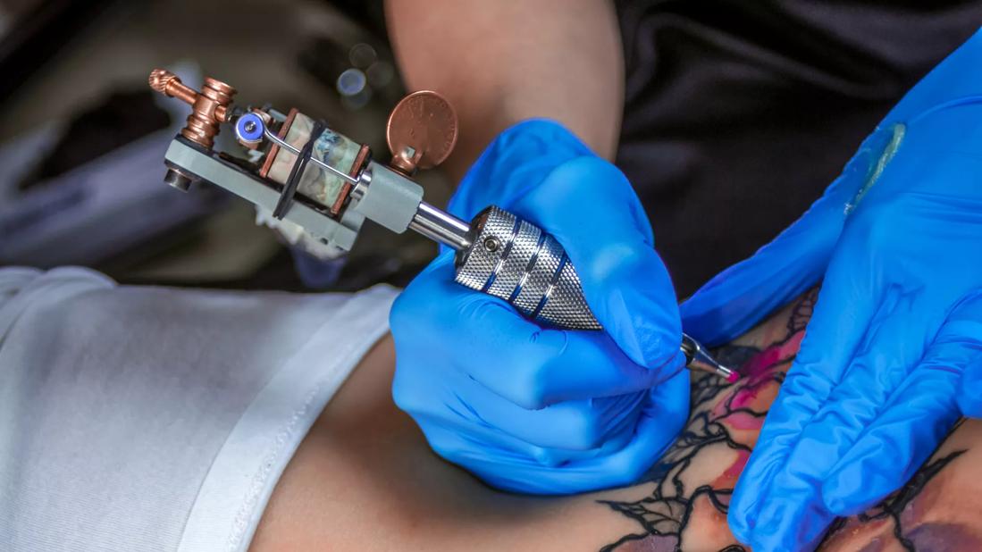 Gloved hands using a tattoo iron to apply a tattoo