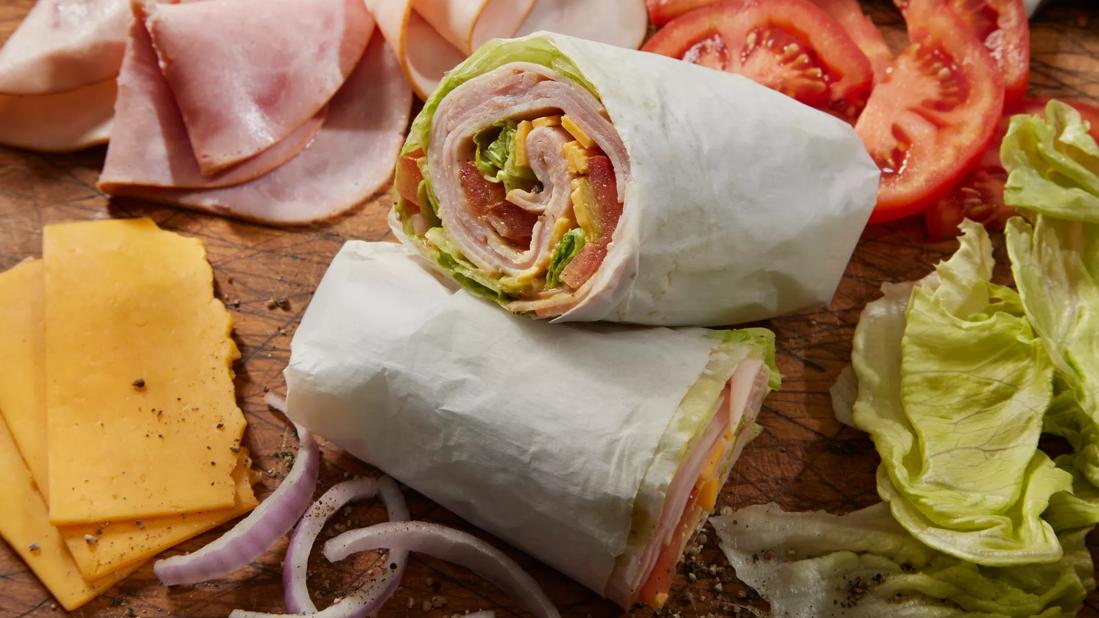 Turkey wrap cut in half on butcher board, with lettuce, tomato, cheese, onion