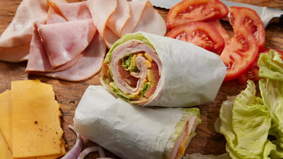 Turkey wrap cut in half on butcher board, with lettuce, tomato, cheese, onion