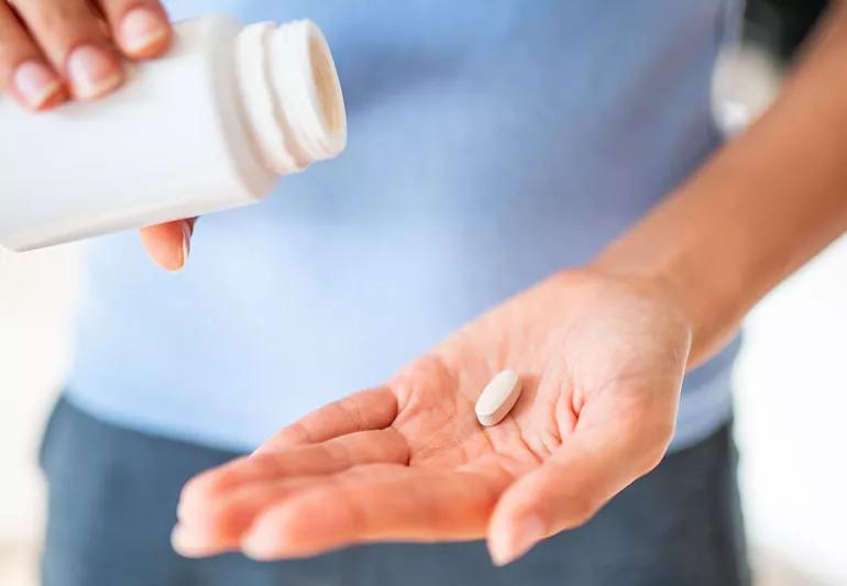 Person with blue shirt is holding vitamin bottle and other hand is holding one vitamin.