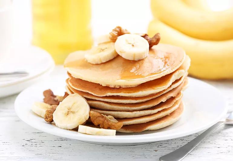 A stack of banana pancakes with syrup and slices of bananas on top