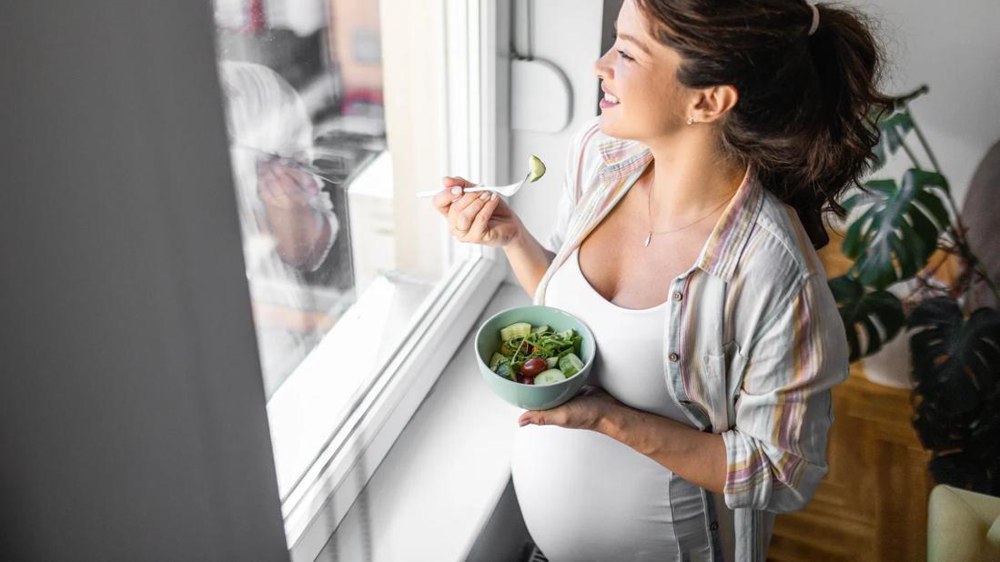 Pregnant woman eating bowl of salad