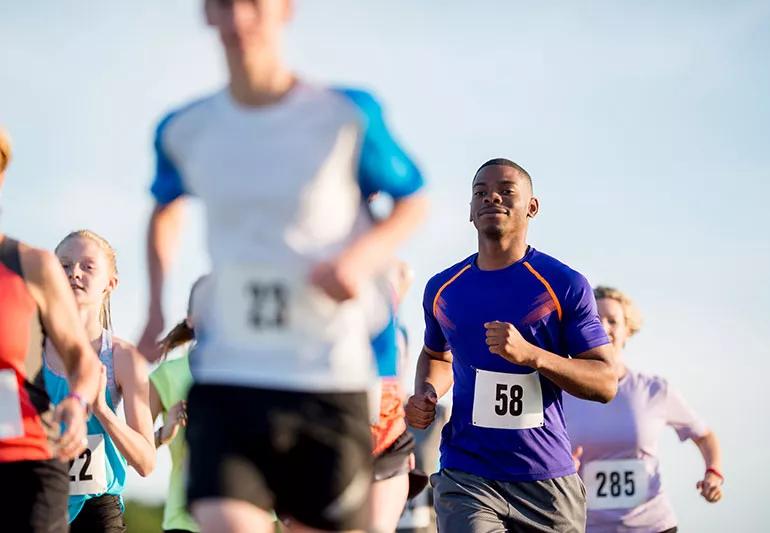 A smiling man running in a race wearing a blue running shirt and a tag with the number 58