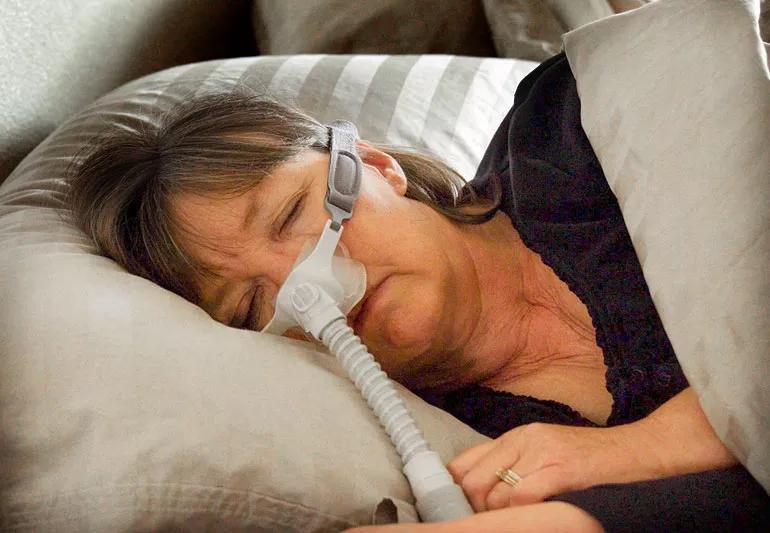 Elderly woman asleep with CPAP positioned over nose.