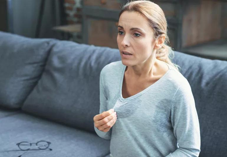 Person sittin on couch suffering from a hot flash, with wet patches showing on shirt.