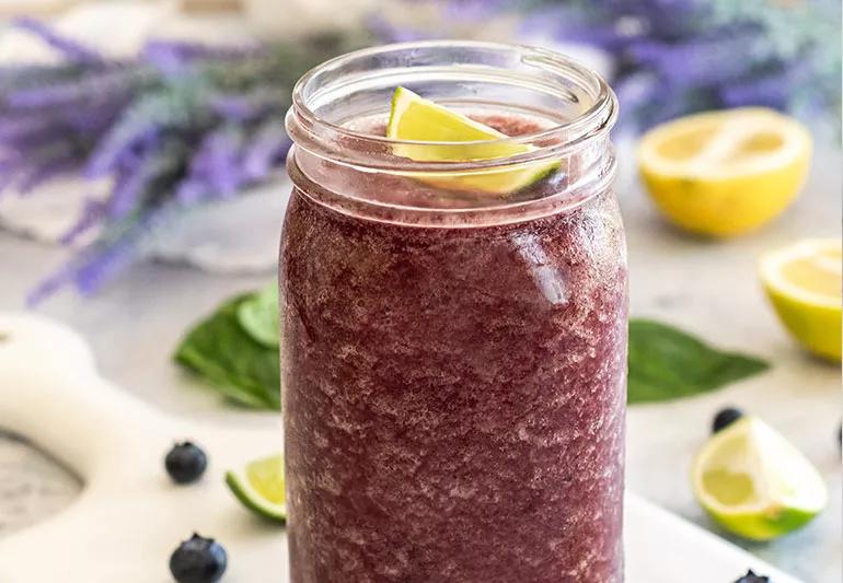 Mason jar filled with berry basil lemonade slushie topped with lime and surrounded by ingredients