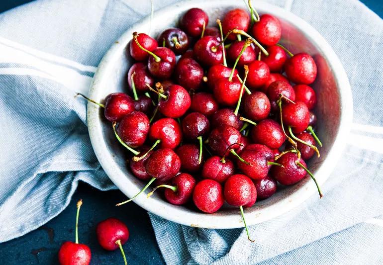 Fresh pickied bowl of cherries in a white bowl on a light blue cloth napkin.