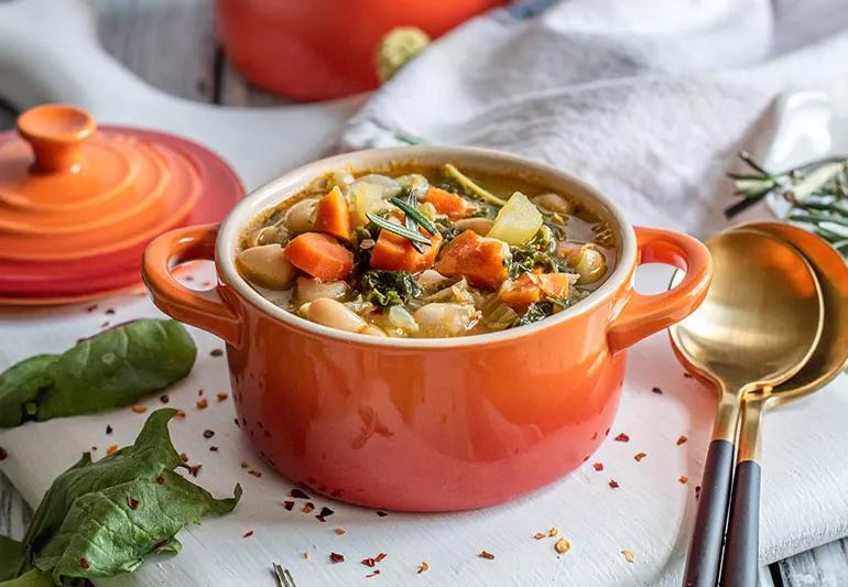 A bright orange ceramic pot full of white bean stew with rosemary and spinach