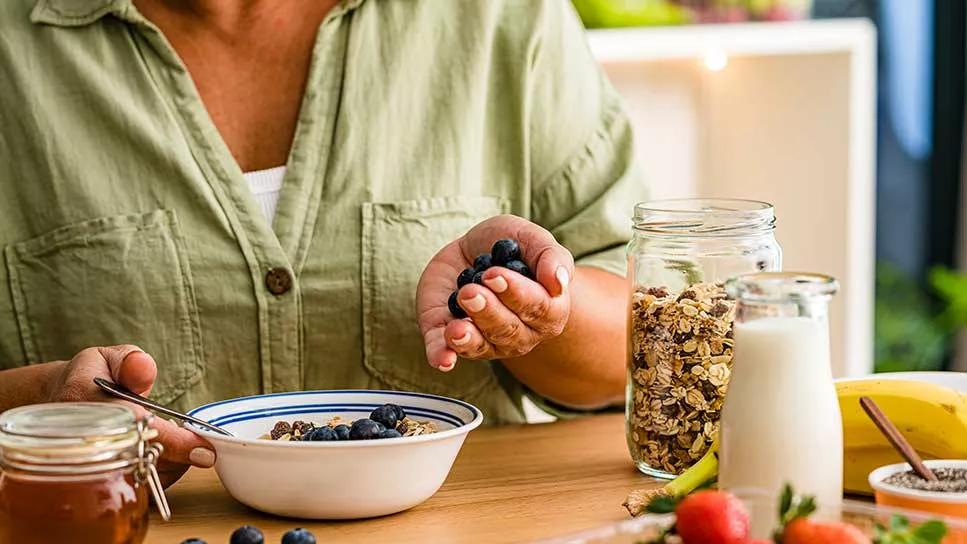 person adding blueberries to bowl of granola cereal