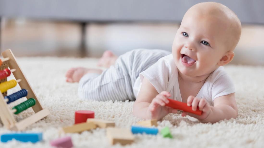 Happy baby on tummy on carpet playing with toys