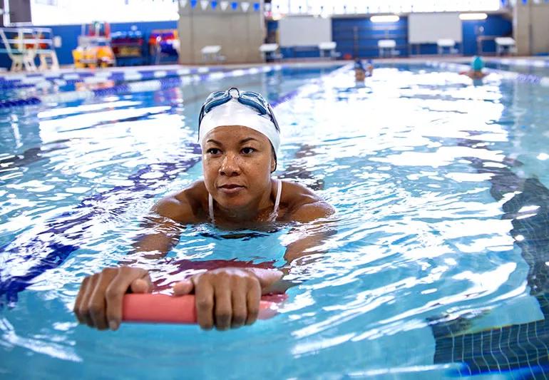 Person swims with flotation device in hands while doing laps at indoor pool.