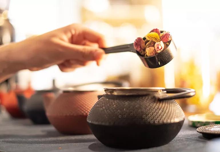 A hand ladling a spoonful of herbs into a pot