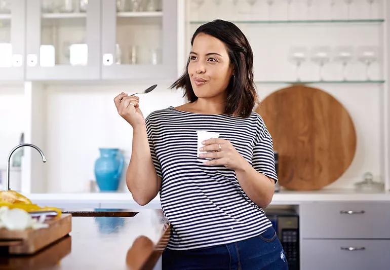 woman eating yogurt while standing in kitchen
