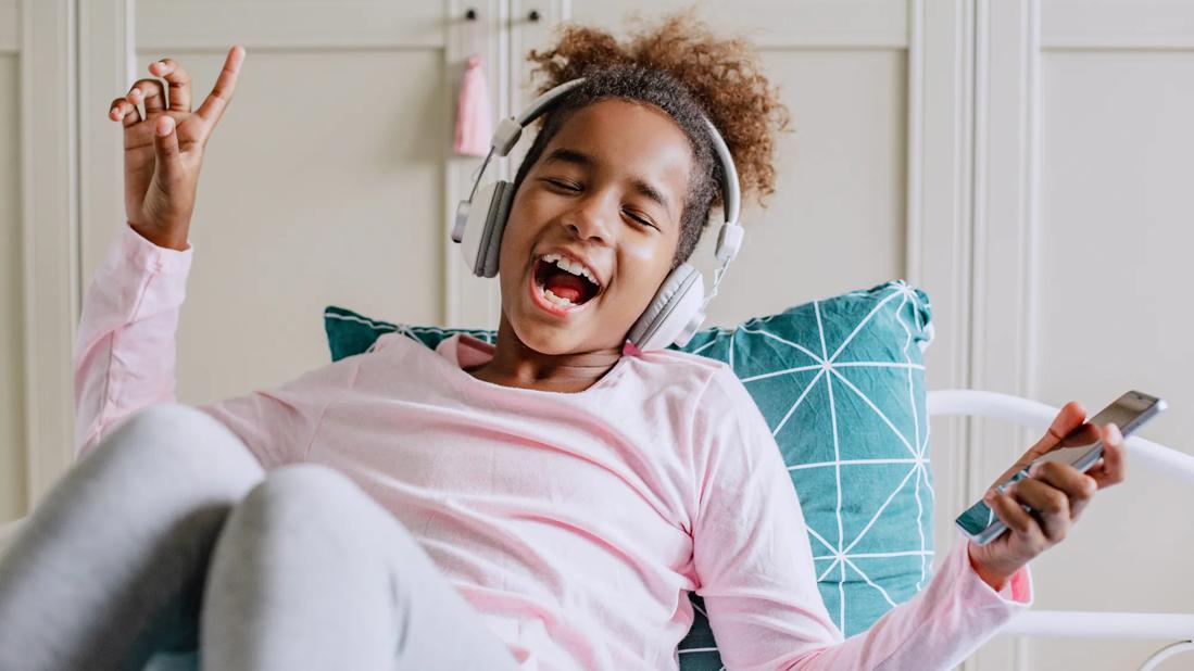 Child on bed and pillow, with over the headphones on, listening to music