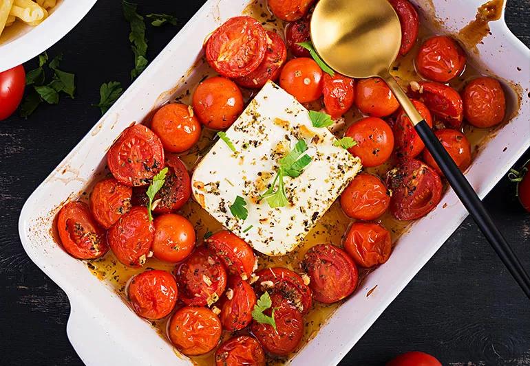 A casserole dish filled with olive oil, grape tomatoes and a brick of feta