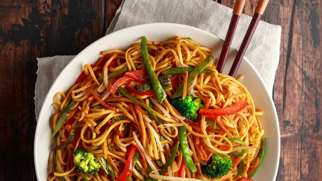 Bowl of Szechwan noodles with broccoli and red pepper, with chopsticks