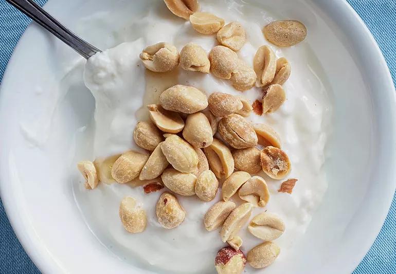 A small white bowl of yogurt with peanuts on top.