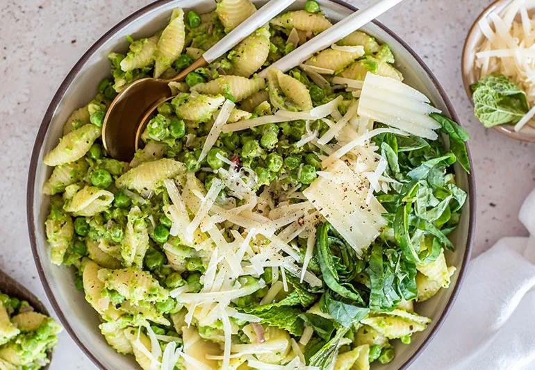 A bowl is full of English pea pasta topped with mint leaves and cheese.
