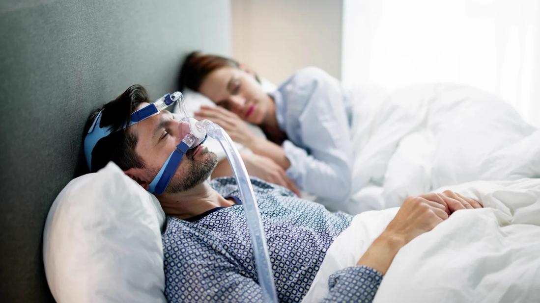 Couple asleep in bed, with one person wearing a CPAP machine mask