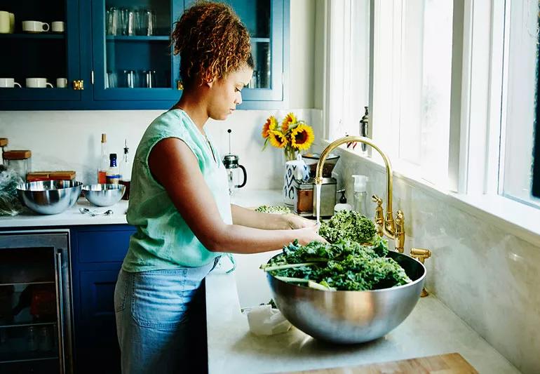 Person washing vegetables in kitchen sink during food preperation.