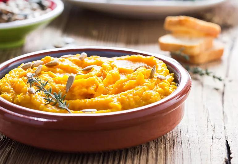 Sweet potato hummus in a terra cota bowl on a wooden table.