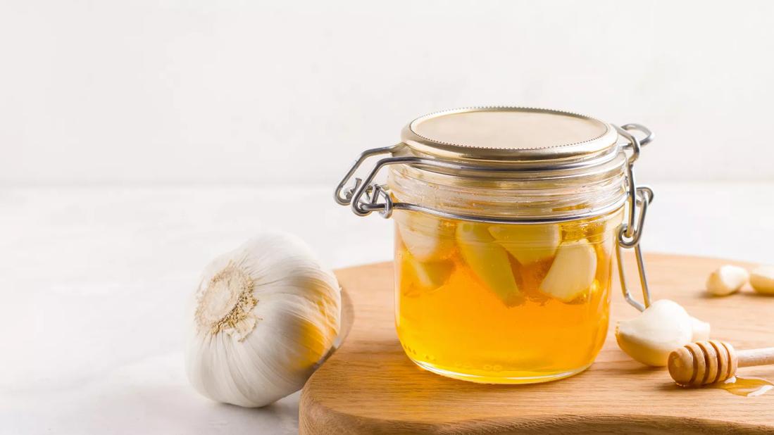 Jar of honey and fresh garlic on cutting board