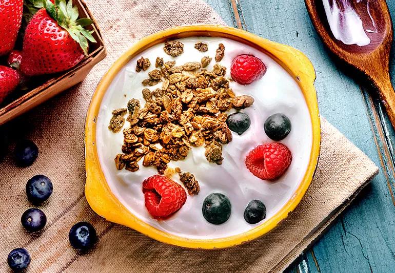 A bowl of yogurt topped with raspberries, blueberres and granola.