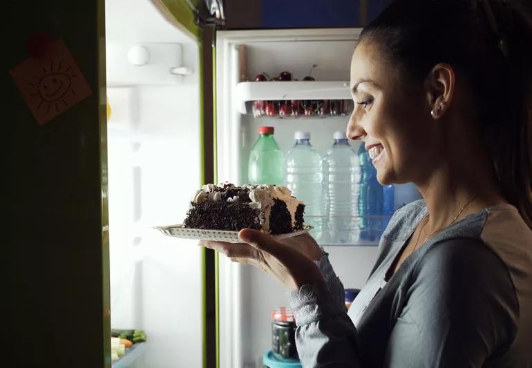 A woman pulling a piece of cake out of her refrigerator.