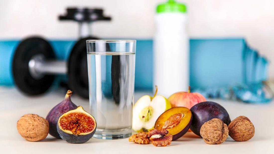 Glass of water and waterbottle, and figs, plums, walnuts and apples, with weights nearby