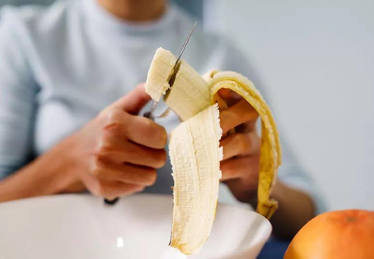 Person cuts banana to add to their breakfast bowl.