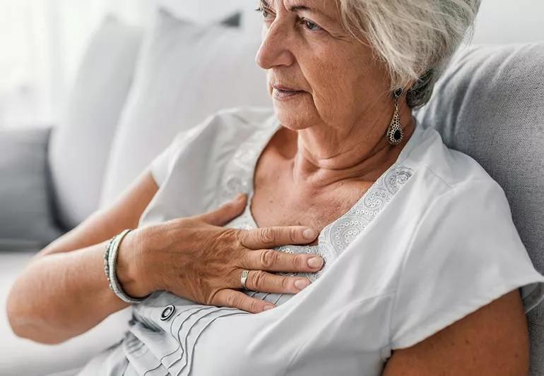 Elderly person on couch with hand on chest suffering from heartburn.