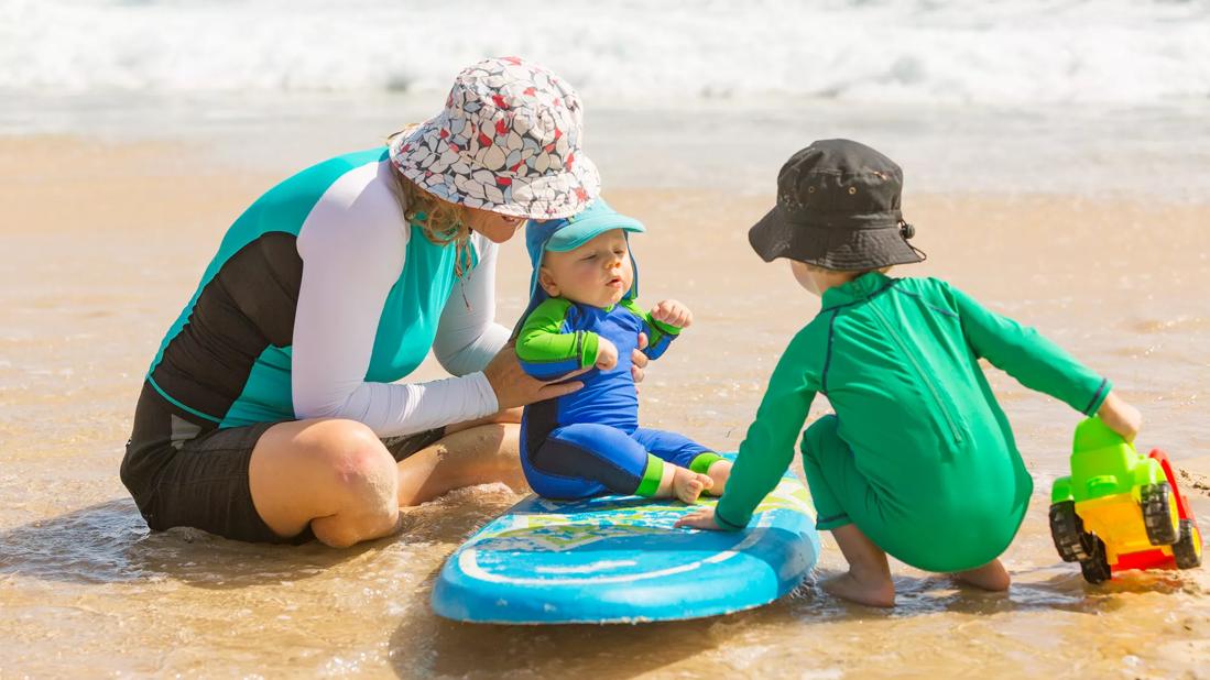 Woman and children wearing UV protective clothes at the beach.