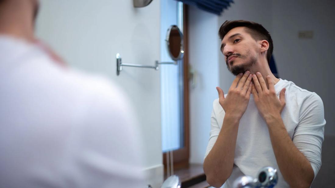 Peson examining their patchy beard in the bathroom mirror