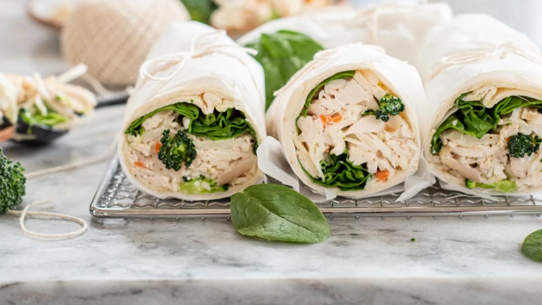 Broccoli slaw chicken wraps wrapped in paper, tied with string on cooling rack on counter