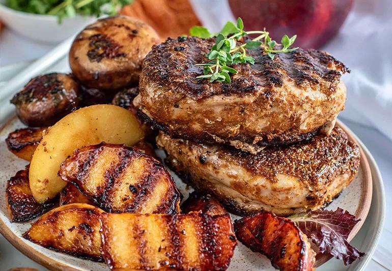 A plate stacked with grilled pork chops and grilled peaches